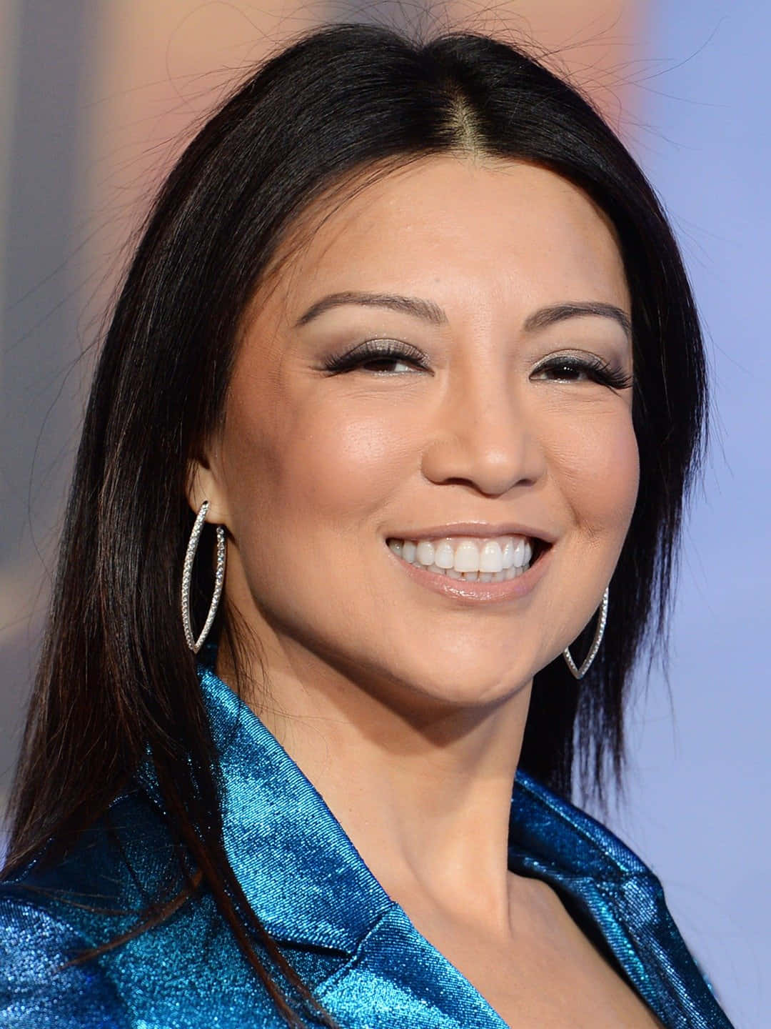 Ming Na Wen 桌布 壁紙 — 一位長黑髮的耀眼女性，穿著閃亮的藍色外套和閃閃發光的圈形耳環，燦爛地微笑。