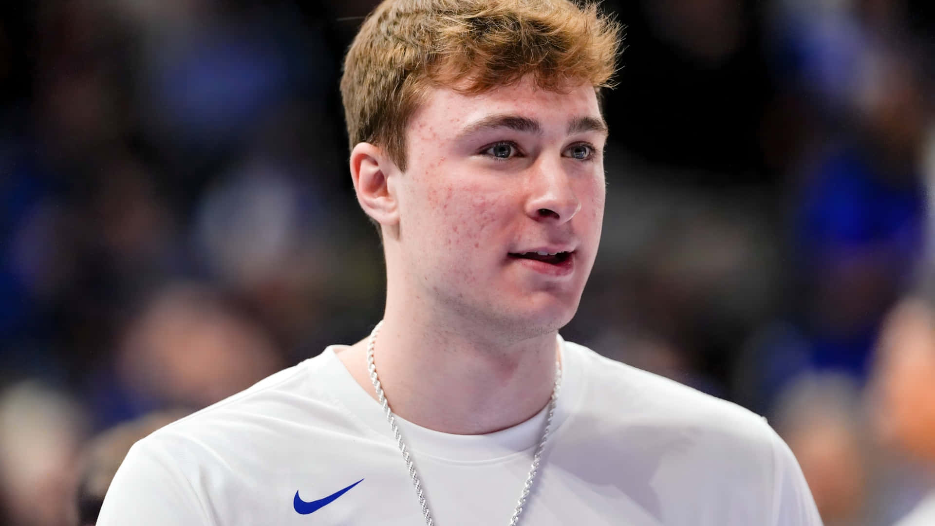  壁紙 — 一位身穿白色Nike球衣、戴著銀色鏈條的年輕籃球運動員，在明亮的場館燈光下比賽時顯得專注。