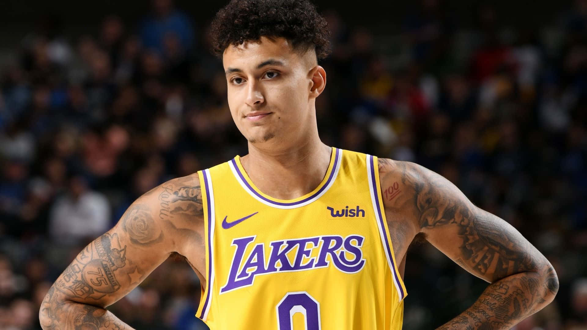  壁紙 — 一位身穿黃色湖人球衣、有紋身的籃球運動員在比賽中自信地雙手叉腰站立。
