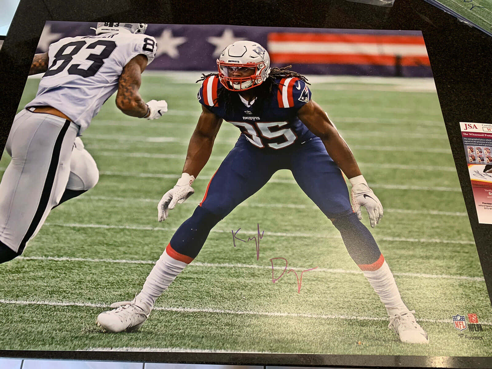  壁紙 — 一位身穿藍色球衣的簽名NFL美式足球員在綠色草地上低蹲，而一位身穿白色球衣的對手正向他衝來。