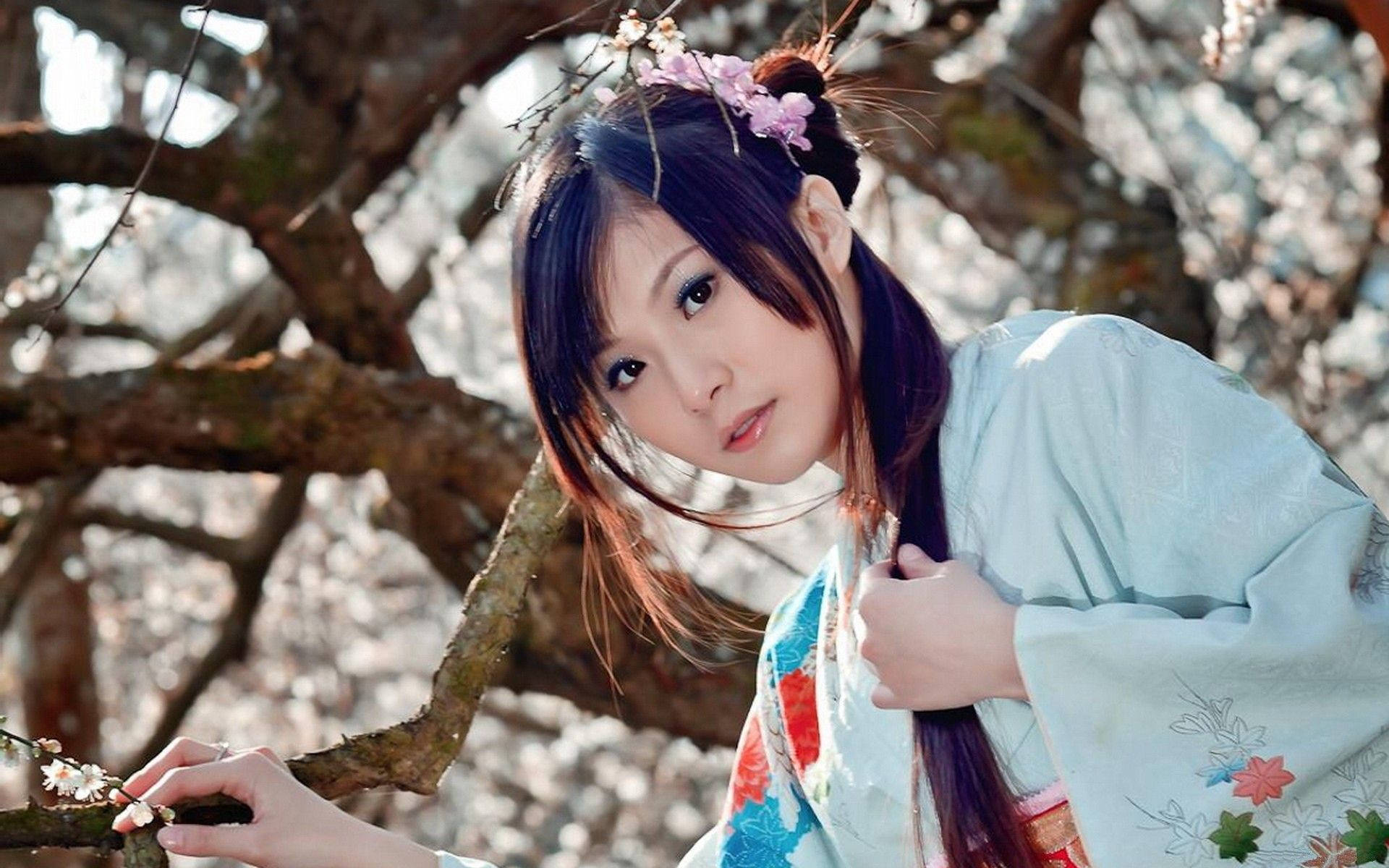 穿著傳統和服的年輕女性觸摸樹枝上的櫻花。