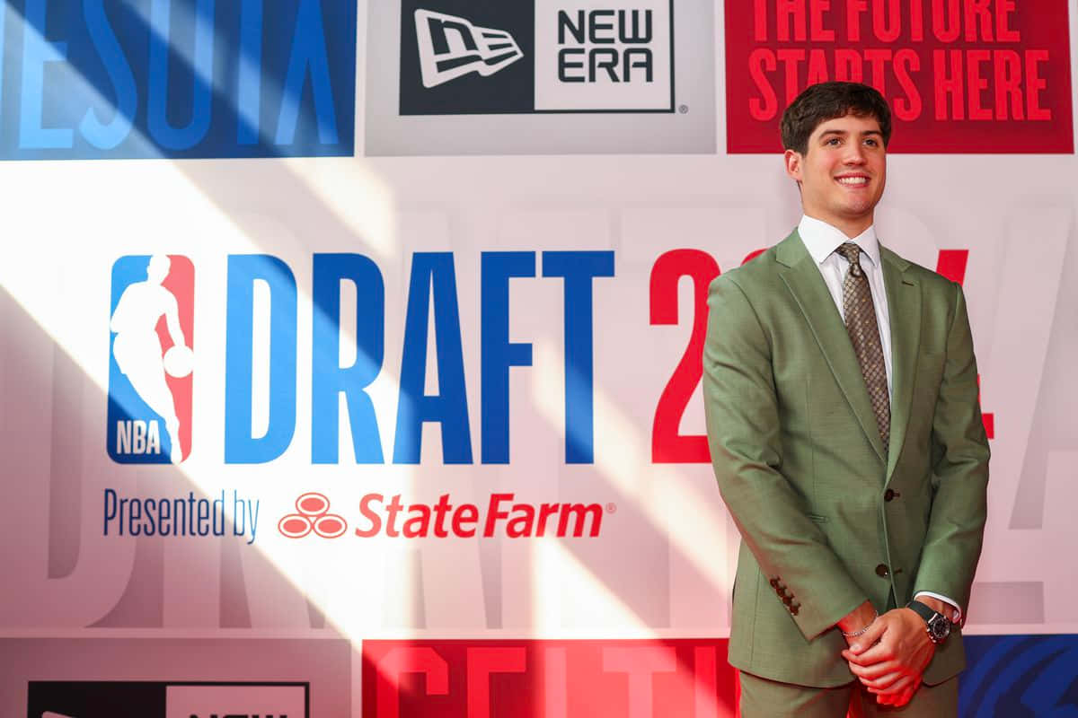  壁紙 — 一位穿著綠色西裝的年輕男子在NBA選秀2024活動背景前自信地微笑，背景上有標誌和粗體文字。