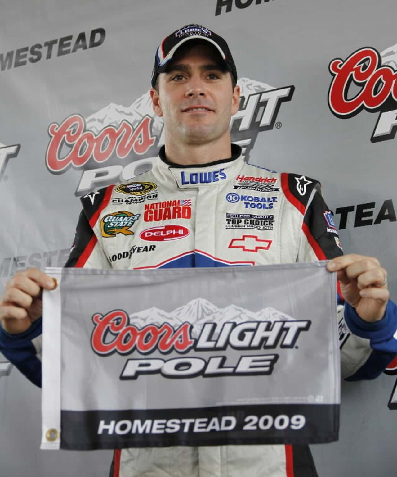 Jimmie Johnson 桌布 壁紙 — 一位穿著贊助商覆蓋的賽車服的NASCAR車手在2009年於Homestead舉著Coors Light Pole獎項旗幟。