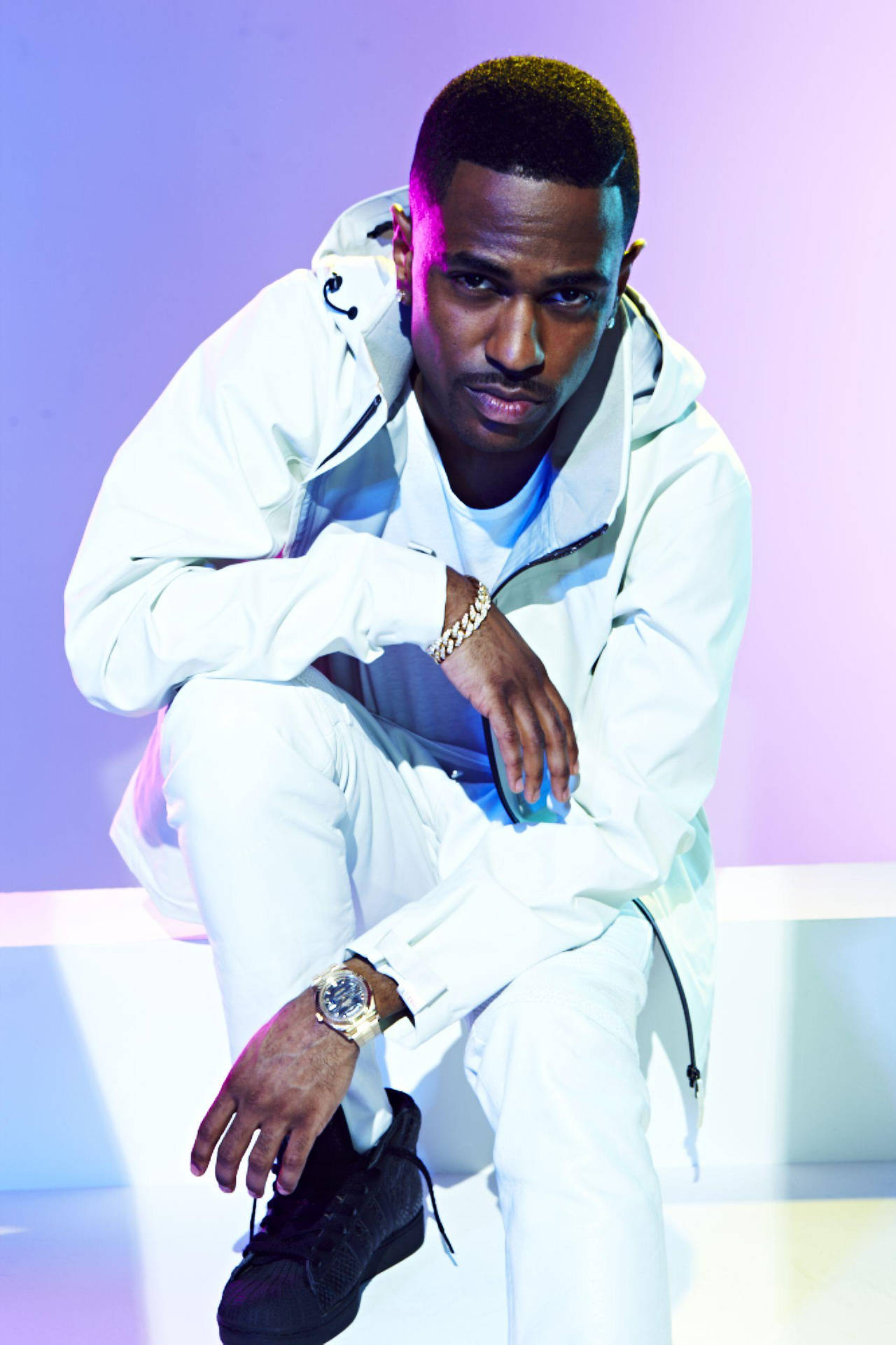 Big Sean 全白造型 壁紙 — 一位穿著白色服裝的時尚男士，自信地蹲在發光的紫色和藍色工作室背景前。