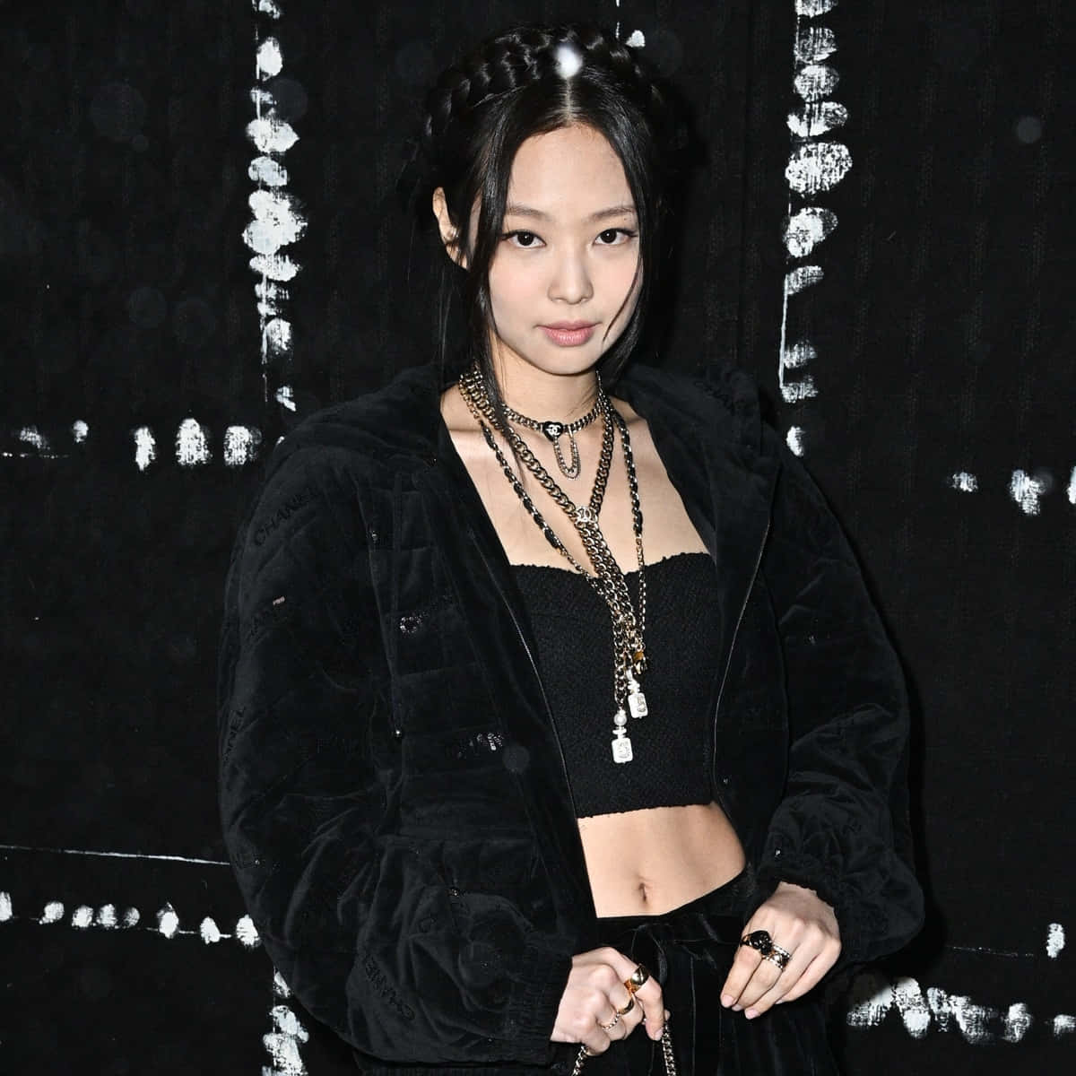 BLACKPINK Jennie 黑色時尚美學照 壁紙 — 一位穿著黑色天鵝絨外套和層疊鏈條的時尚女性，在帶有紋理的黑白背景前擺姿勢。