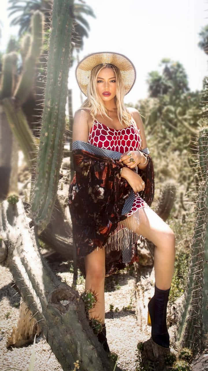  壁紙 — 一位戴著草帽、身穿圖案連衣裙的女性在明亮的沙漠陽光下，自信地站在高大的薩瓜羅仙人掌中擺姿勢。