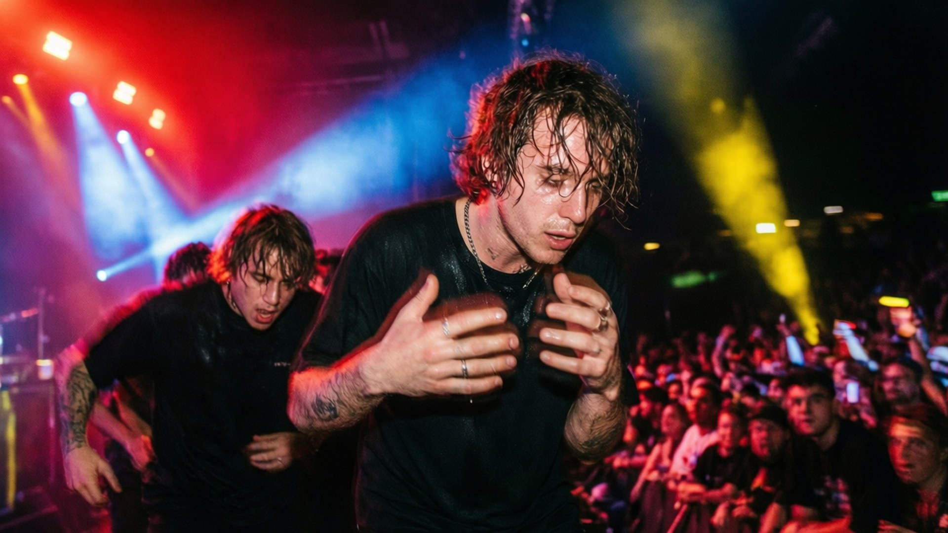Brockhampton 桌布 壁紙 — 一位汗流浹背的音樂家在充滿活力的紅、藍、黃燈光下，在舞台上激烈表演，身後擠滿了人群。