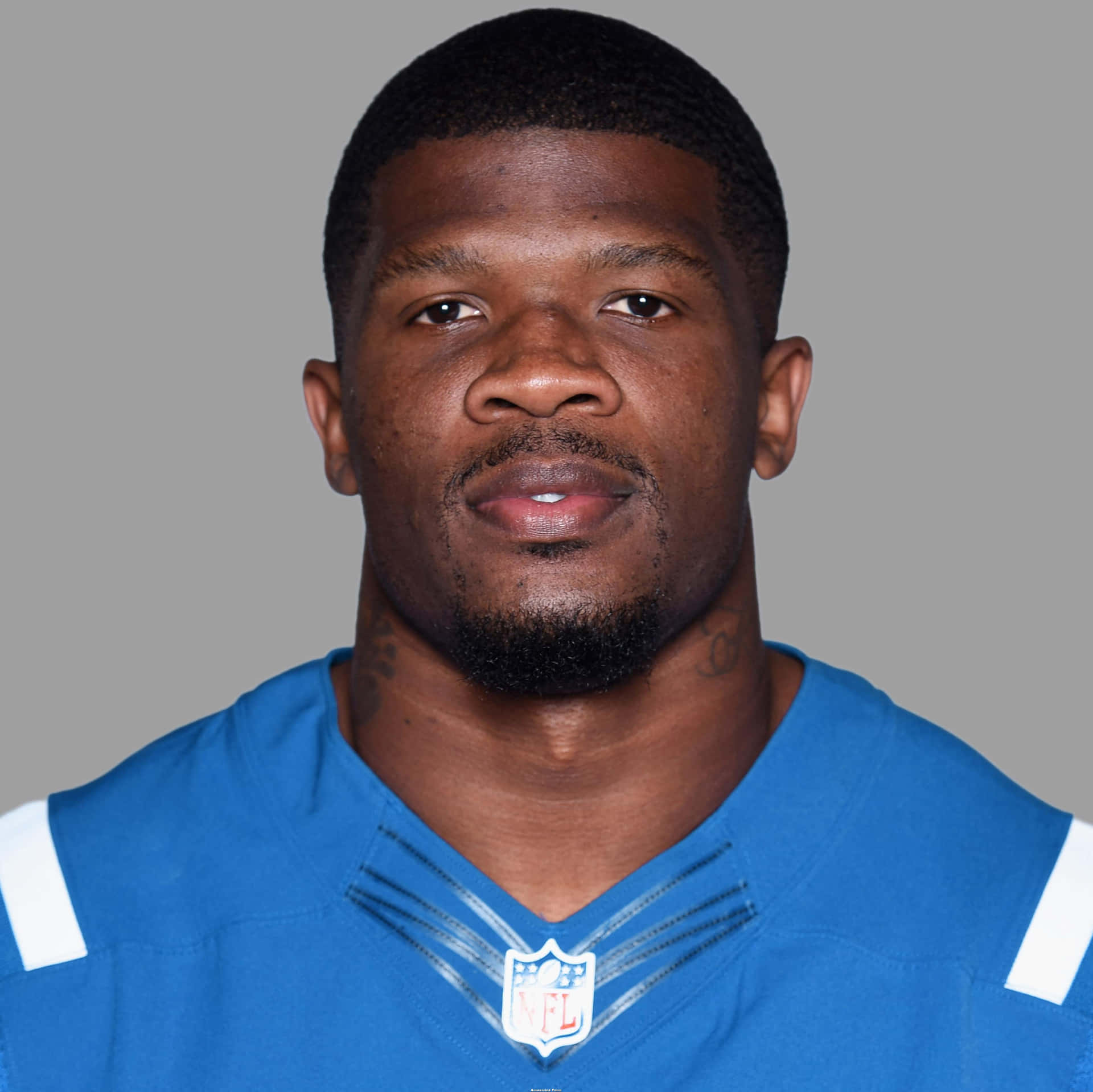  壁紙 — 一位黑人NFL美式足球運動員的近距離肖像，身穿帶有白色條紋和NFL標誌的藍色球衣，背景為中性灰色。