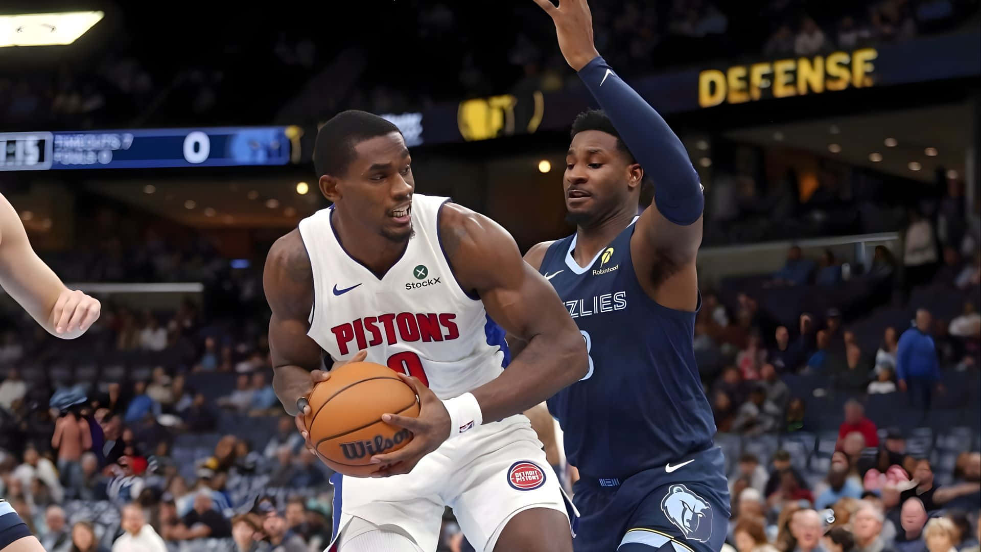  壁紙 — 一位活塞隊球員在球場燈光下，於緊張的NBA比賽中越過灰熊隊防守球員。