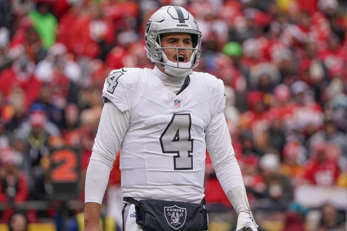  壁紙 — 一位堅定的NFL四分衛身穿白色Raiders球衣4號，在日間比賽中大喊，身後是模糊的紅色人群。