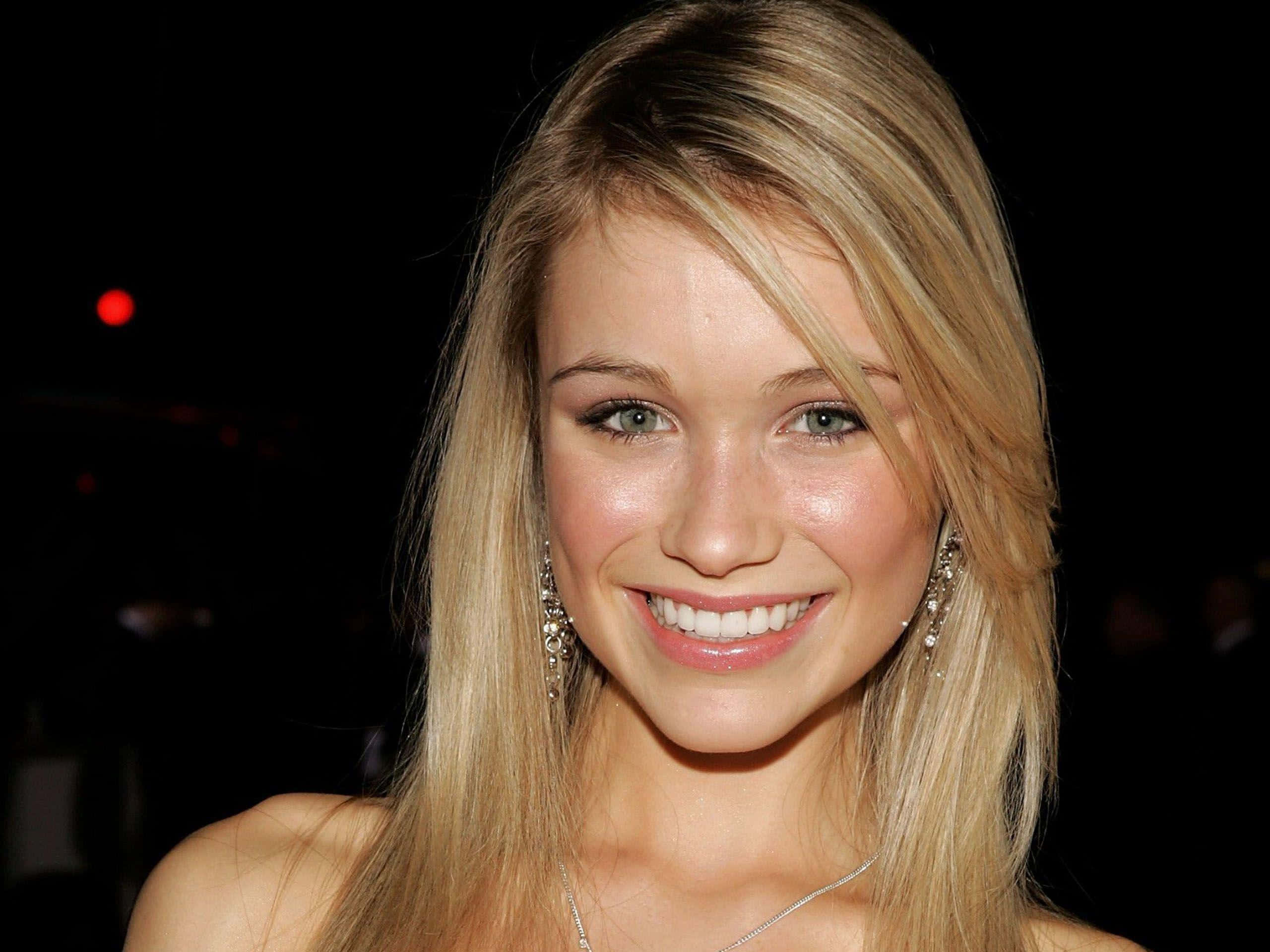 Katrina Bowden 桌布 壁紙 — 一位金髮碧眼、閃閃發光的女性在黑暗背景中，伴隨著柔和散景燈光，溫暖地微笑。
