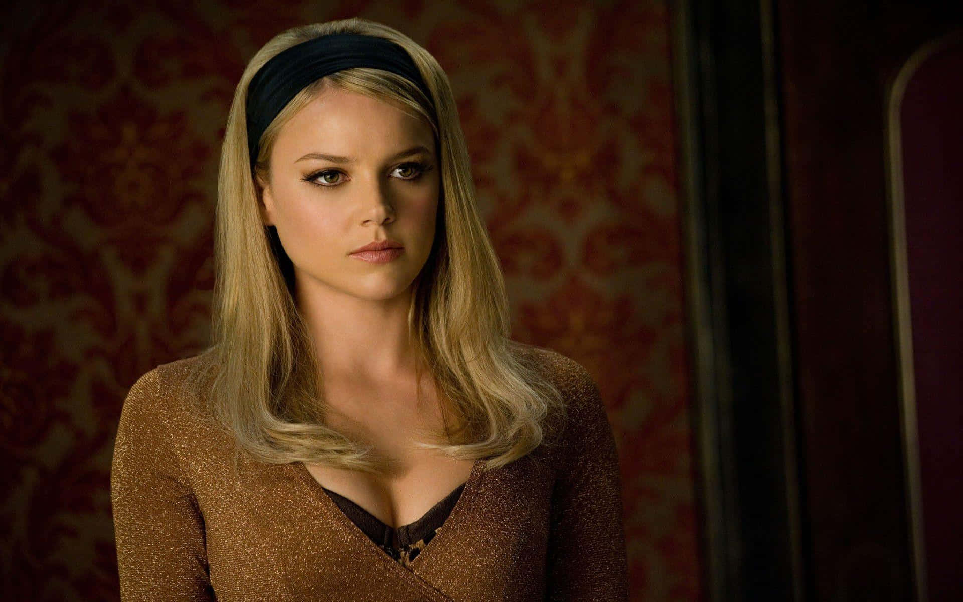 Abbie Cornish 桌布 壁紙 — 一位金髮戴黑色頭帶的女子，在濃郁的紅色錦緞牆紙背景下凝視著。