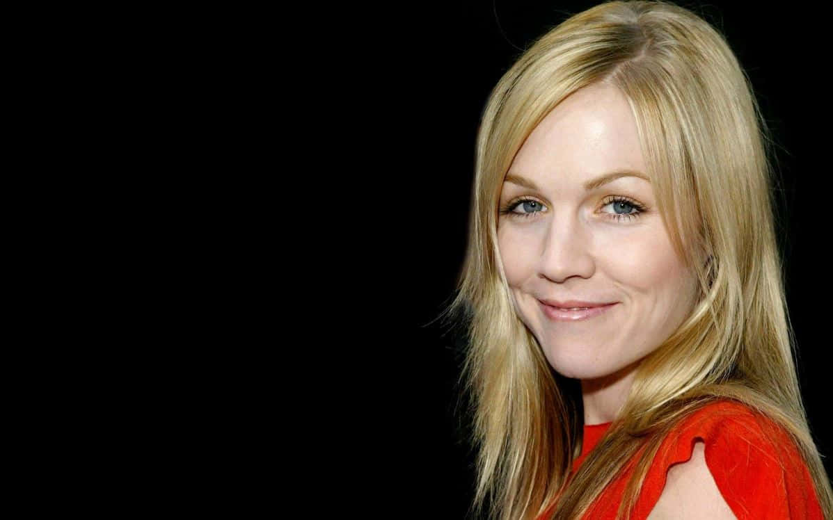 Jennie Garth 桌布 壁紙 — 一位金髮藍眼的女性在黑色背景前穿著紅色上衣溫柔微笑。