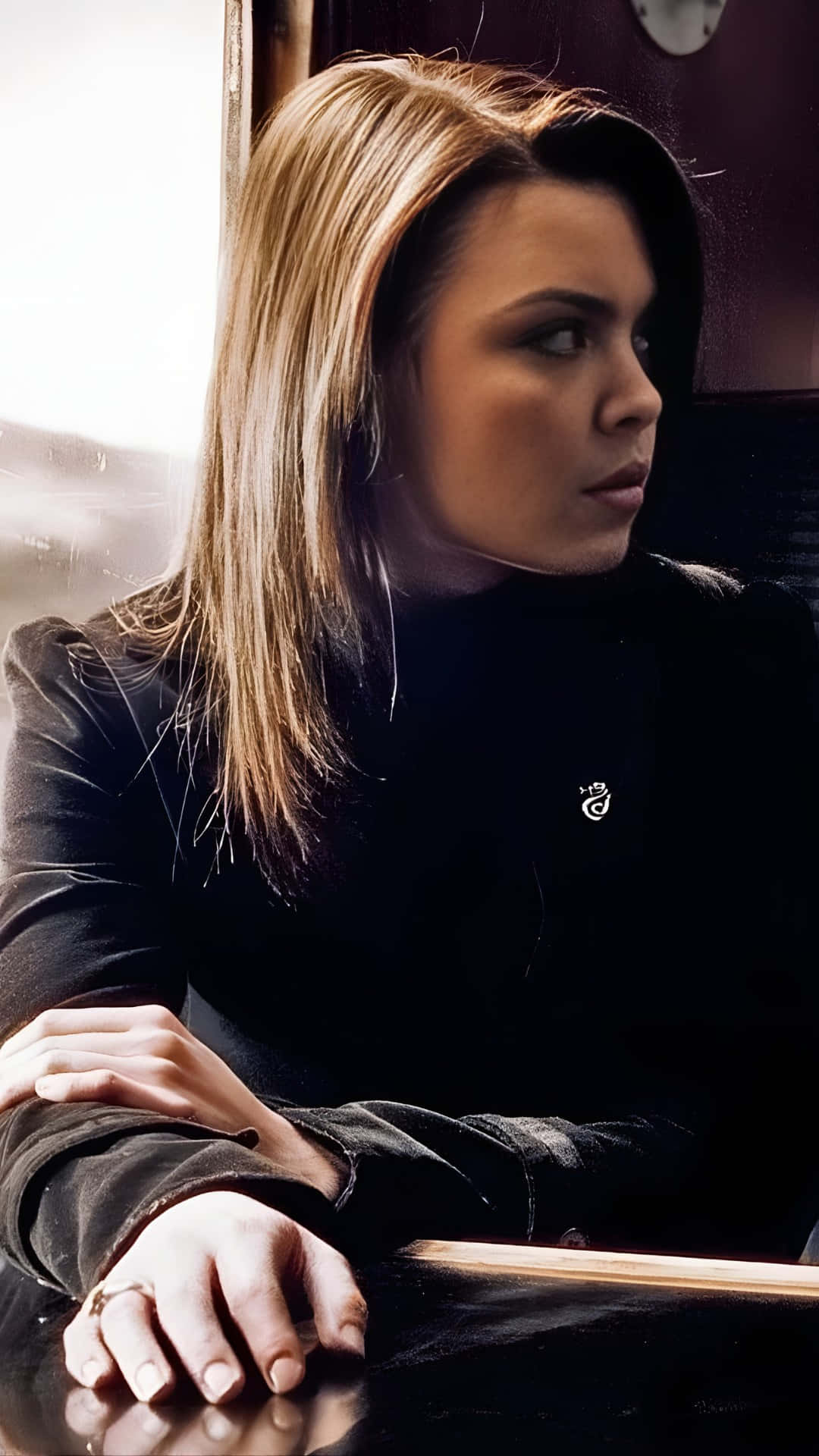  壁紙 — 一位金髮女性穿著黑色高領毛衣，若有所思地望著火車窗外。
