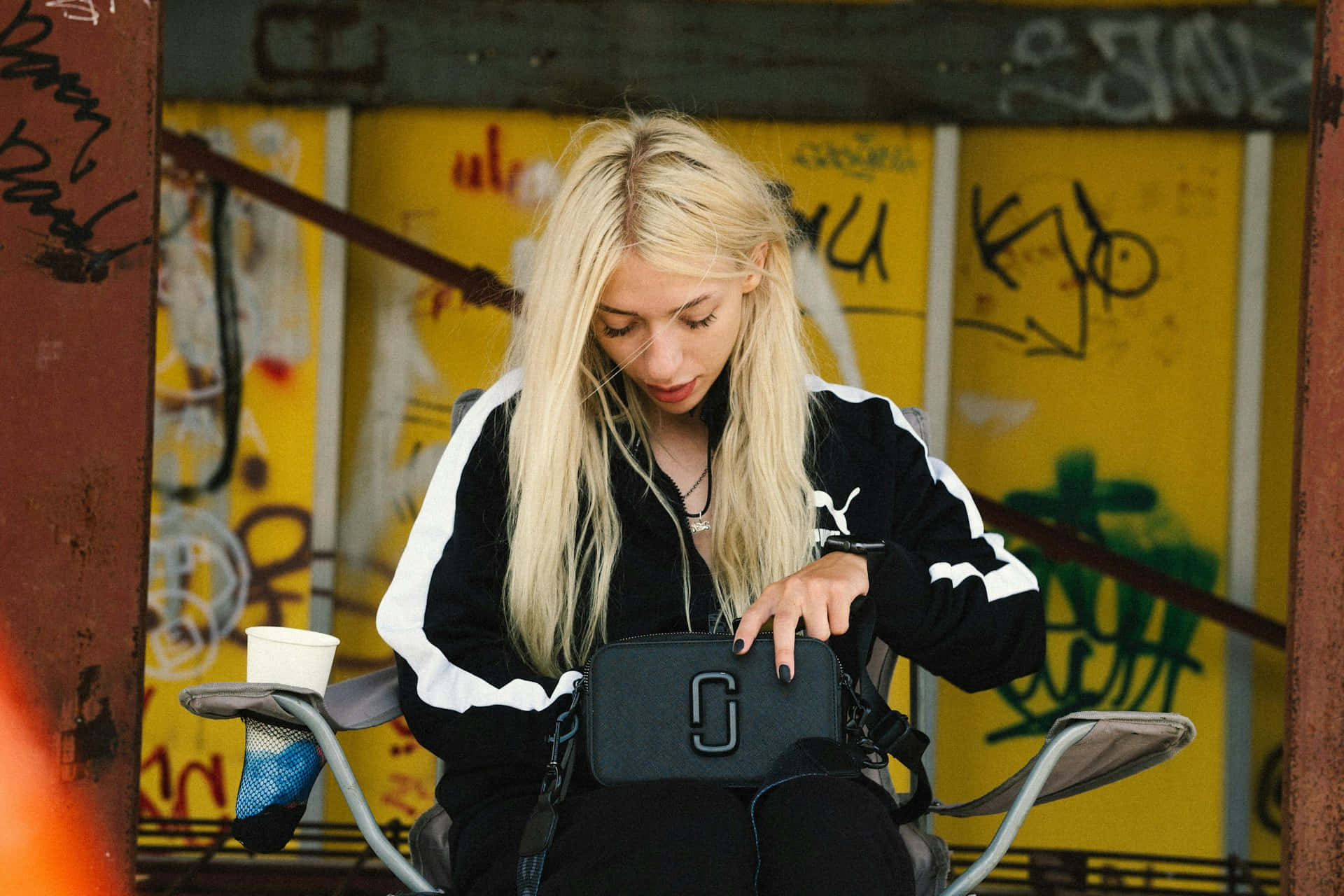  壁紙 — 一位金髮女子穿著黑白運動服坐在單車上，手持黑色手袋，背景是充滿活力的黃色塗鴉牆。