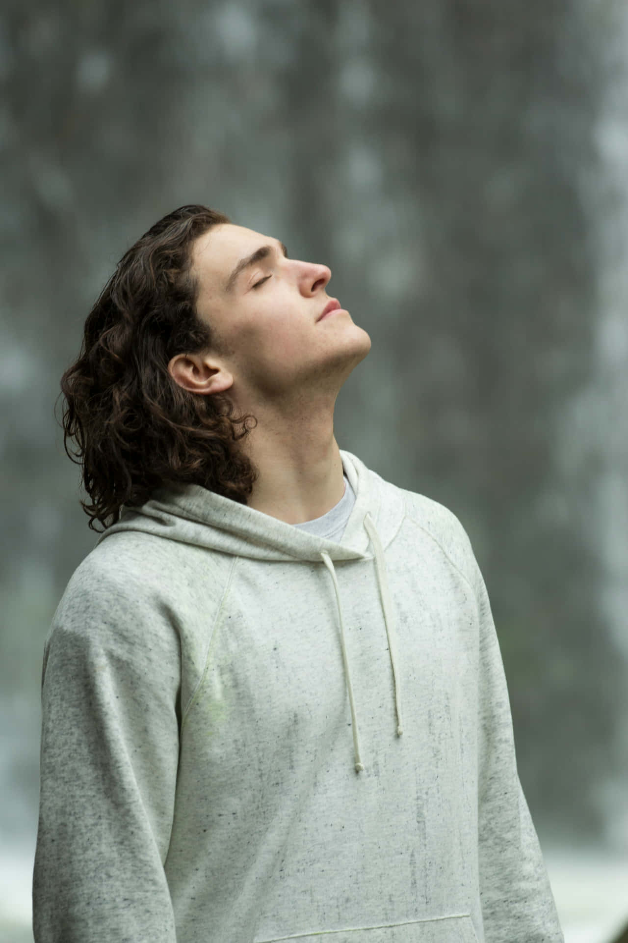  壁紙 — 一位捲髮年輕男子閉上眼睛，在模糊的森林背景下向後仰頭，享受寧靜的放鬆。