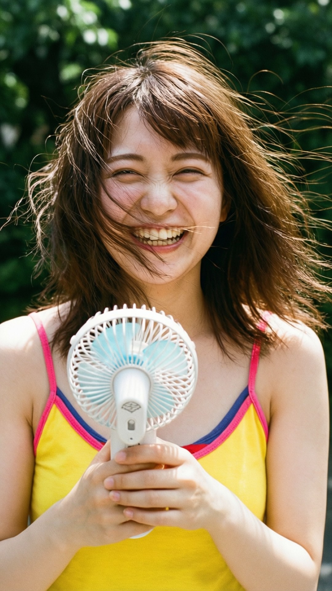 Momo 桌布 壁紙 — 一位開心的年輕女子在戶外大笑，頭髮被風吹起，手持一把手持扇。