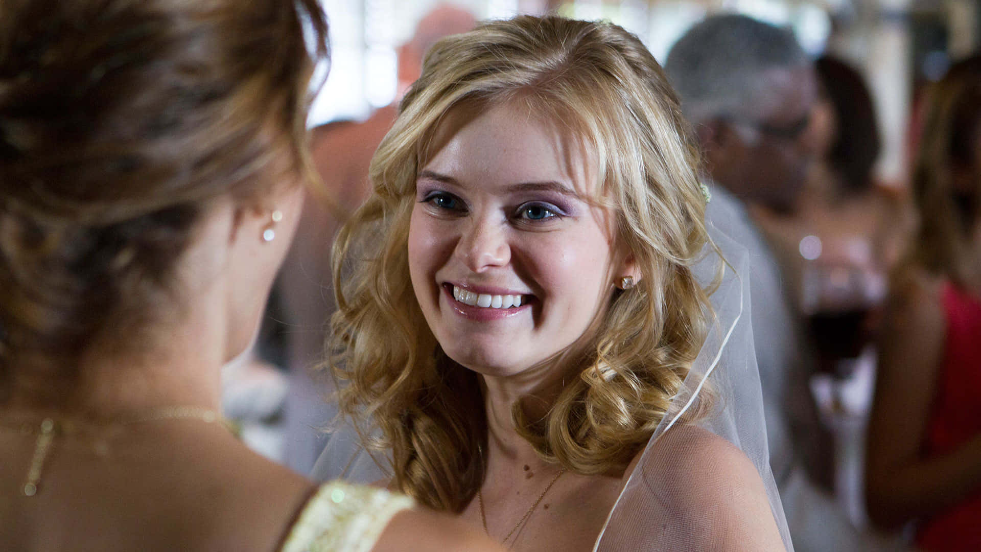 Sara Paxton 桌布 壁紙 — 一位快樂的金髮新娘戴著頭紗，在婚宴上擁抱另一位女士，洋溢著幸福。