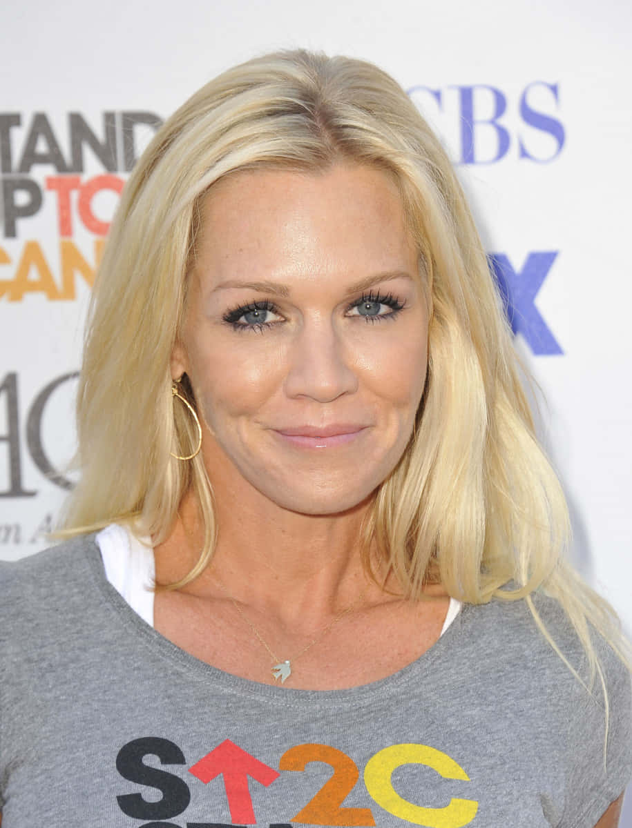Jennie Garth 桌布 壁紙 — 一位藍眼睛的金髮女性在CBS活動中穿著帶有彩色文字的灰色T恤，溫柔地微笑。