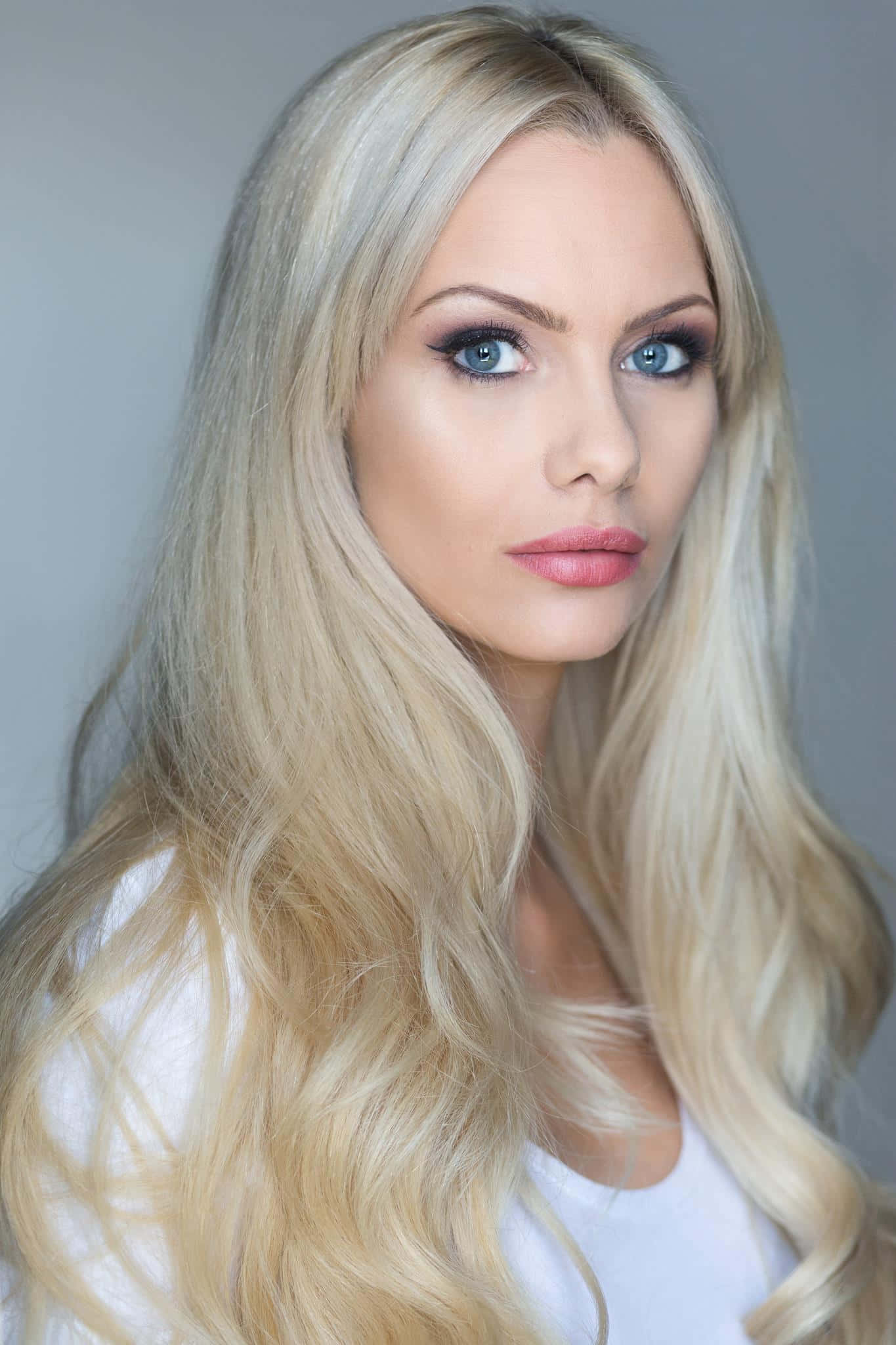 Jessica Jane Clement 桌布 壁紙 — 一位令人驚豔的金髮女郎，擁有銳利的藍色眼睛，在柔和的灰色背景下直視鏡頭。