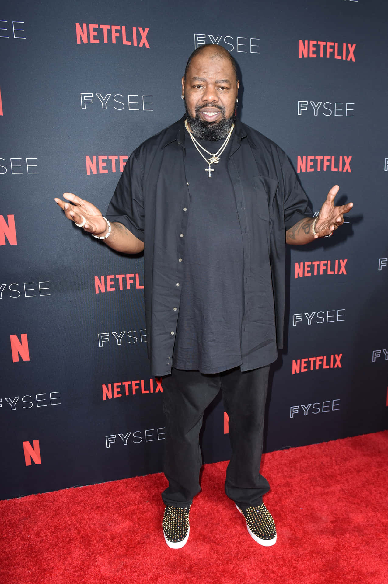  壁紙 — 一位留鬍鬚的男人站在紅地毯上，背景是黑色，上面重複出現Netflix和FYSEE標誌。