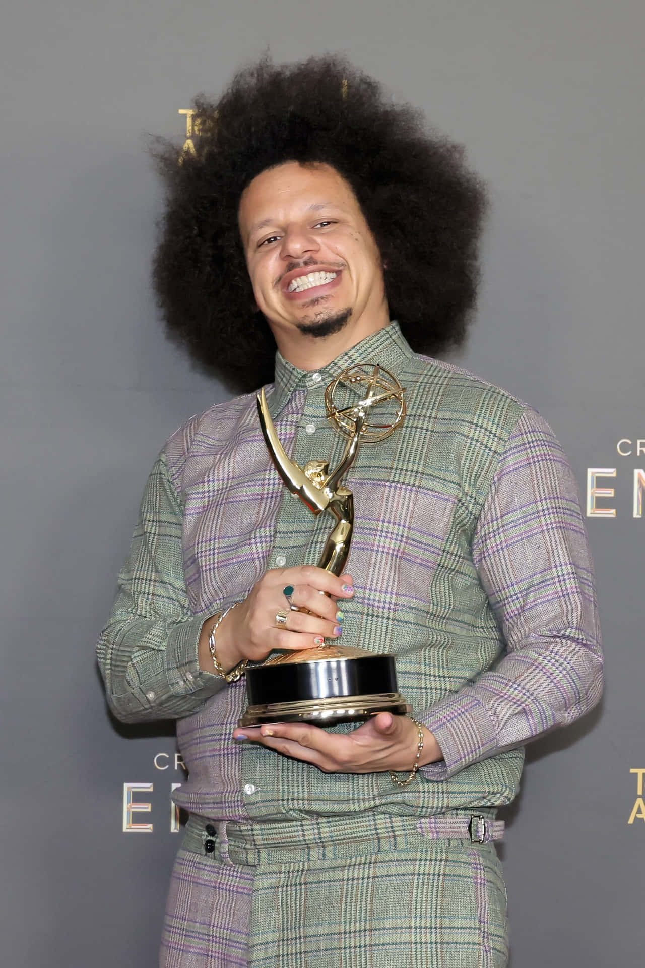  壁紙 — 一位留著大爆炸頭的男人在正式活動中微笑著手持金色艾美獎。