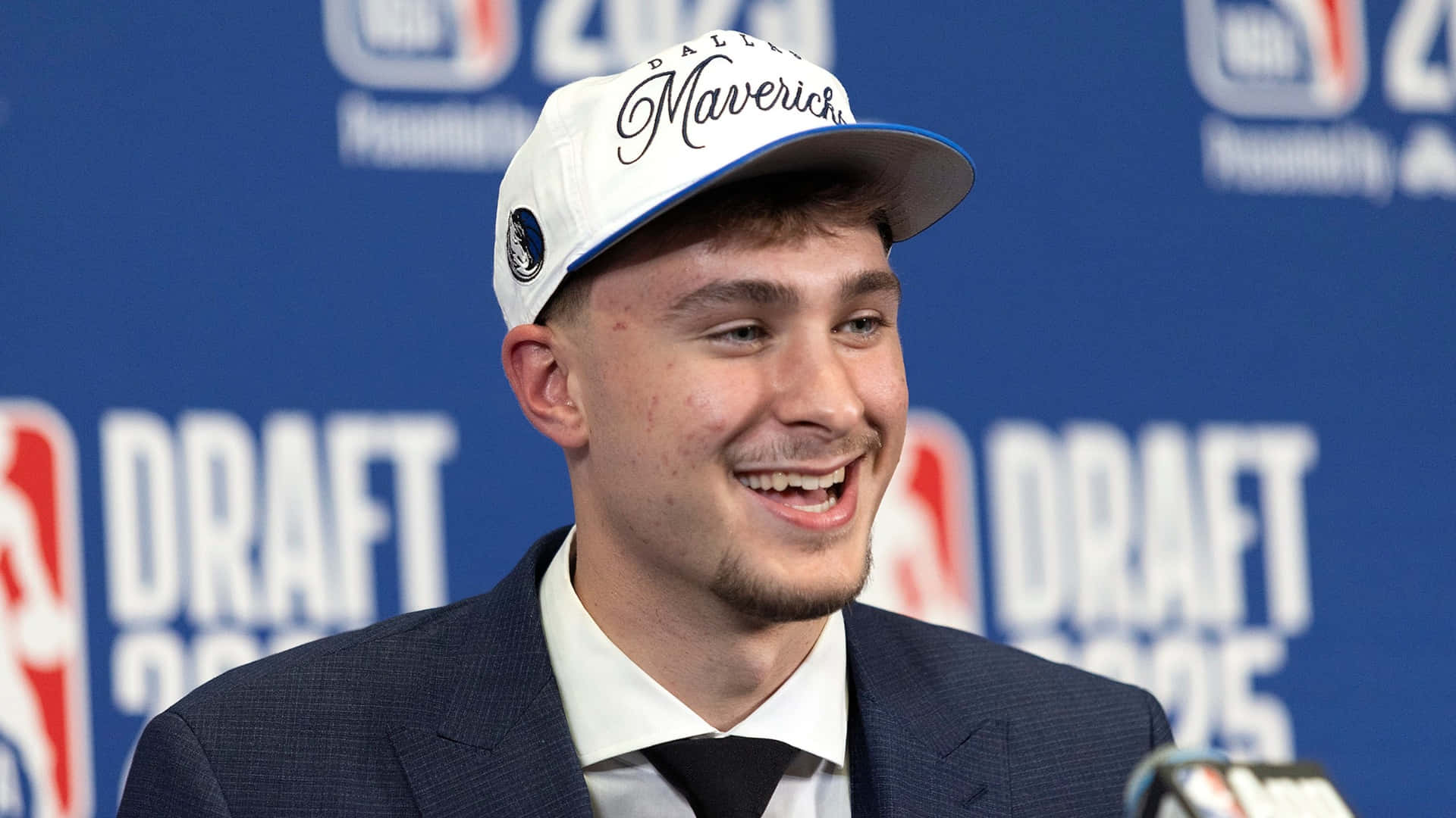  壁紙 — 一位年輕籃球運動員戴著達拉斯獨行俠隊帽，在NBA選秀記者會上喜氣洋洋。