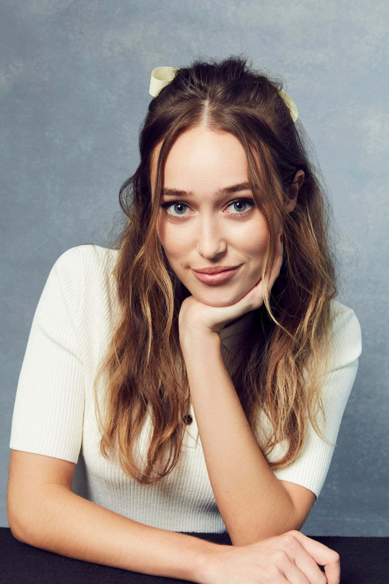 alycia debnam carey 桌布 壁紙 — 一位年輕女性，波浪形棕色頭髮，戴著白色蝴蝶結，在柔和的灰色背景下，用手托著下巴。