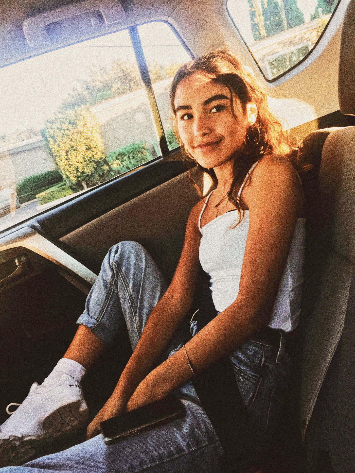  壁紙 — 一位年輕女性坐在車後座，沐浴在金色的午後陽光中，露出溫暖的笑容。