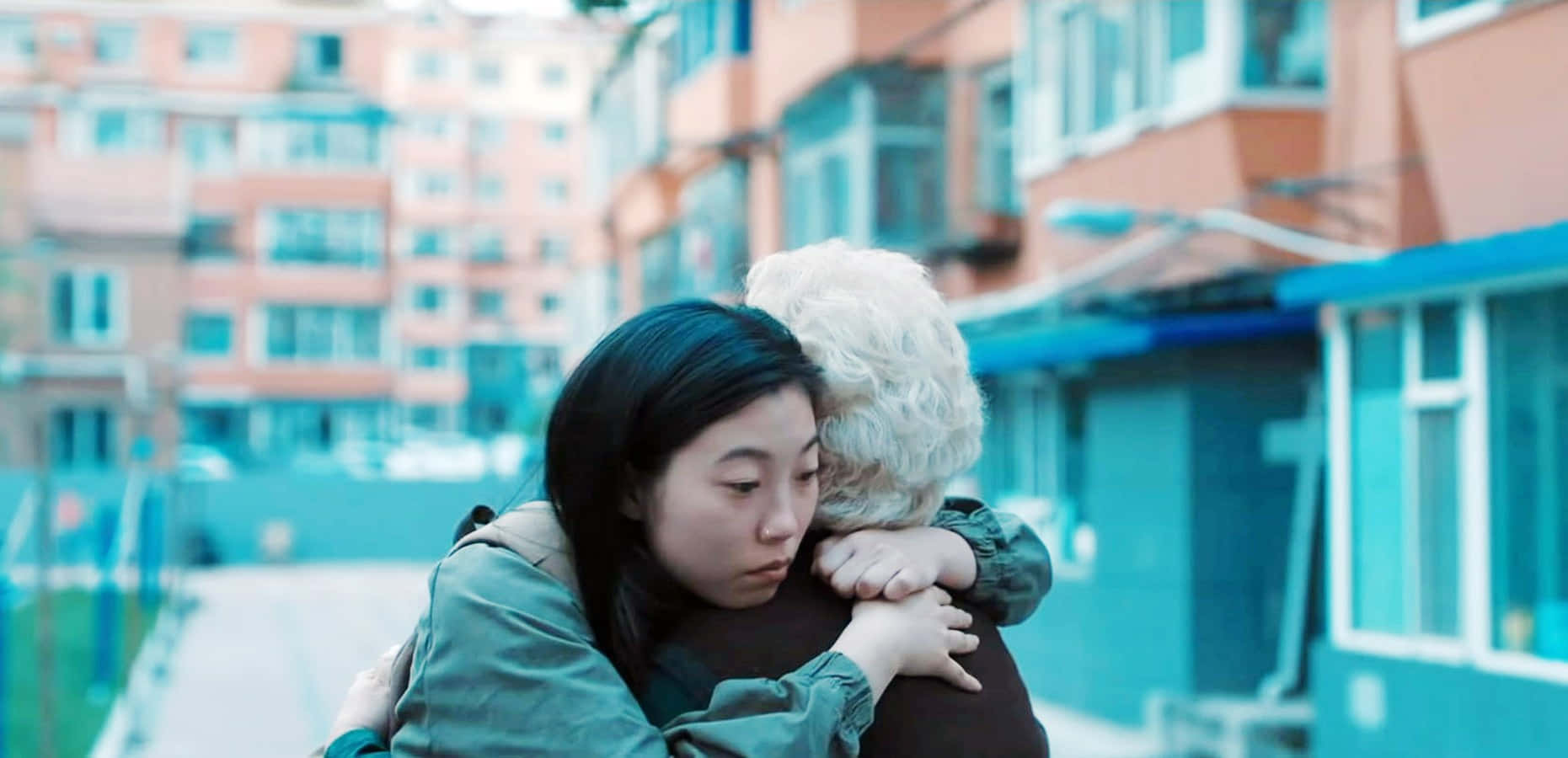 The Farewell 桌布 壁紙 — 一位年輕女子在色彩繽紛的公寓大樓背景下，溫柔地擁抱一位年長女子。