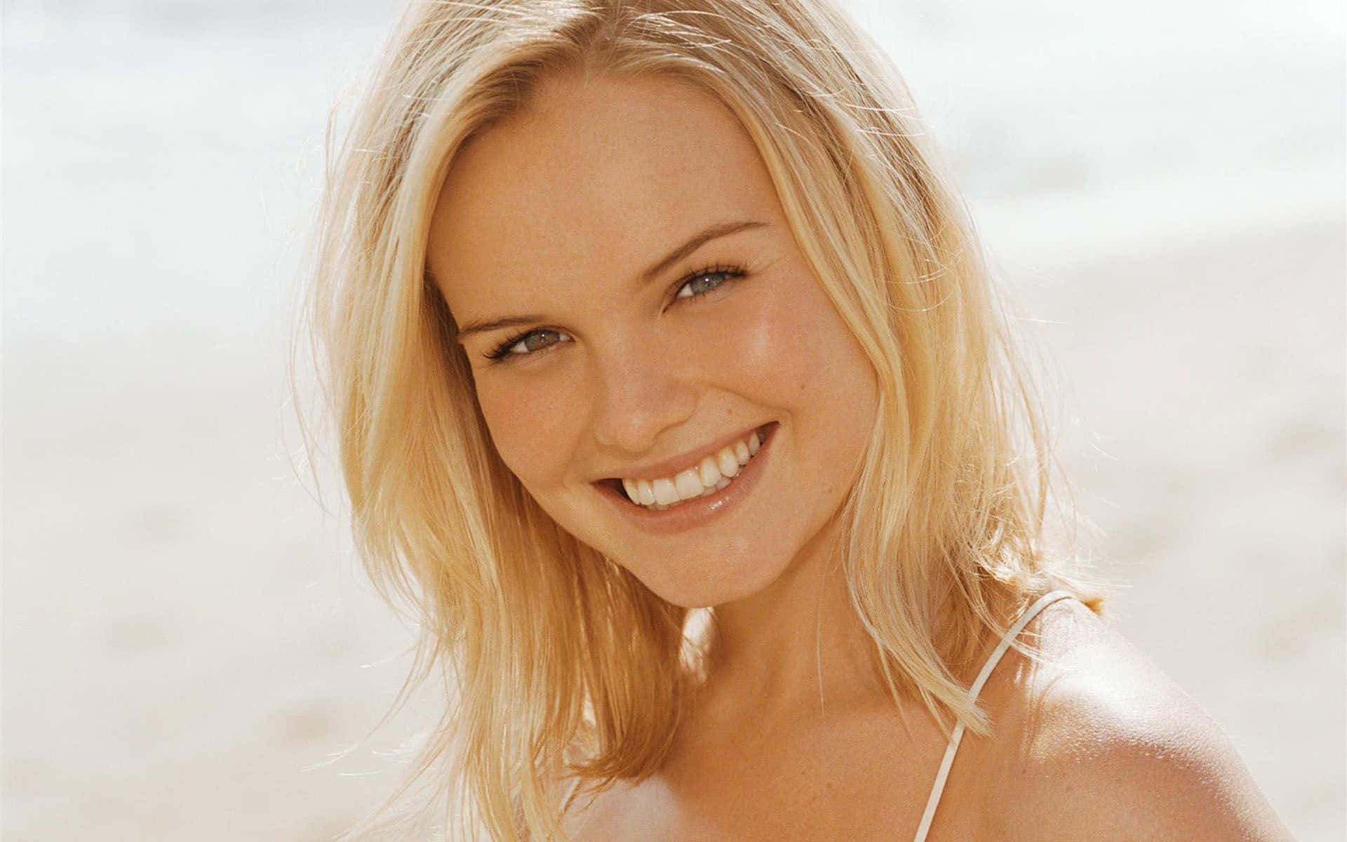 Kate Bosworth 桌布 壁紙 — 一位容光煥發的金髮女性在明亮的沙灘背景下溫暖地微笑。