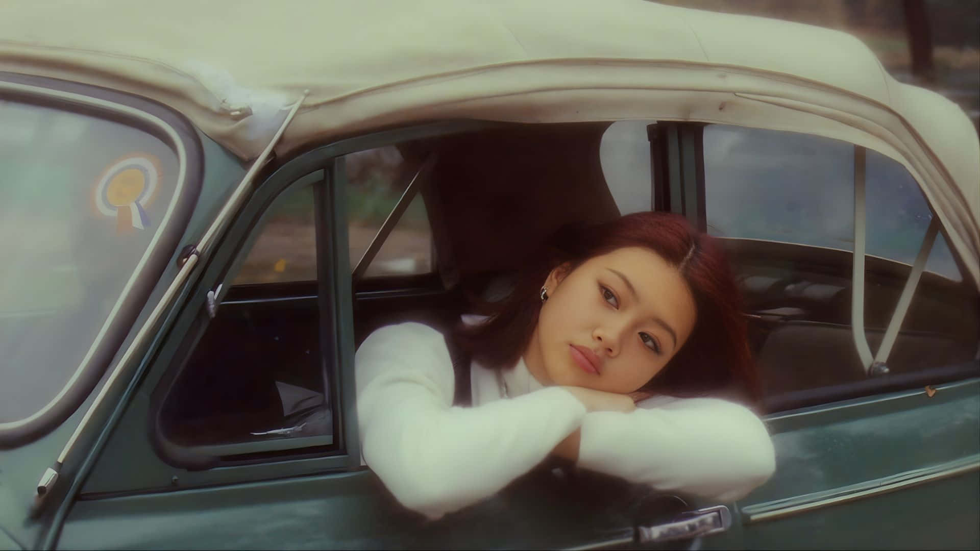  壁紙 — 一位身穿白色毛衣的年輕女子，將頭探出奶油色車頂的復古綠色汽車窗外。