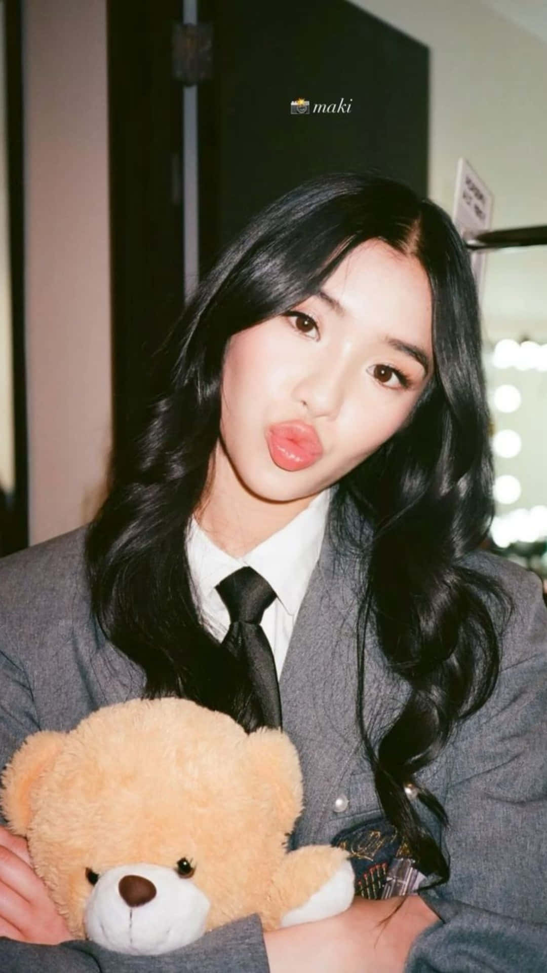  壁紙 — 一位身穿灰色西裝、留著黑色長髮的年輕女性，俏皮地嘟起嘴唇，抱著一隻棕色的泰迪熊。