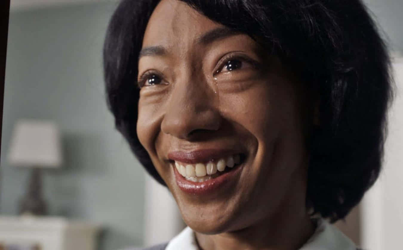  壁紙 — 一位深色頭髮的快樂女性在柔和光線的室內環境中露出燦爛的笑容，露出牙齒和瞇起的眼睛。