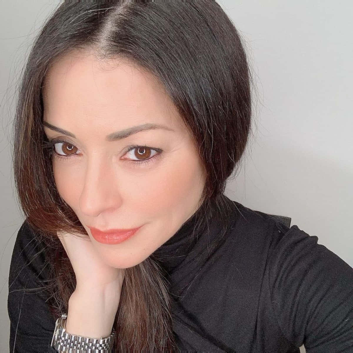 Emmanuelle Vaugier 桌布 壁紙 — 一位深色頭髮、溫暖棕色眼睛的女性，在純淺灰色背景上用手托著下巴。