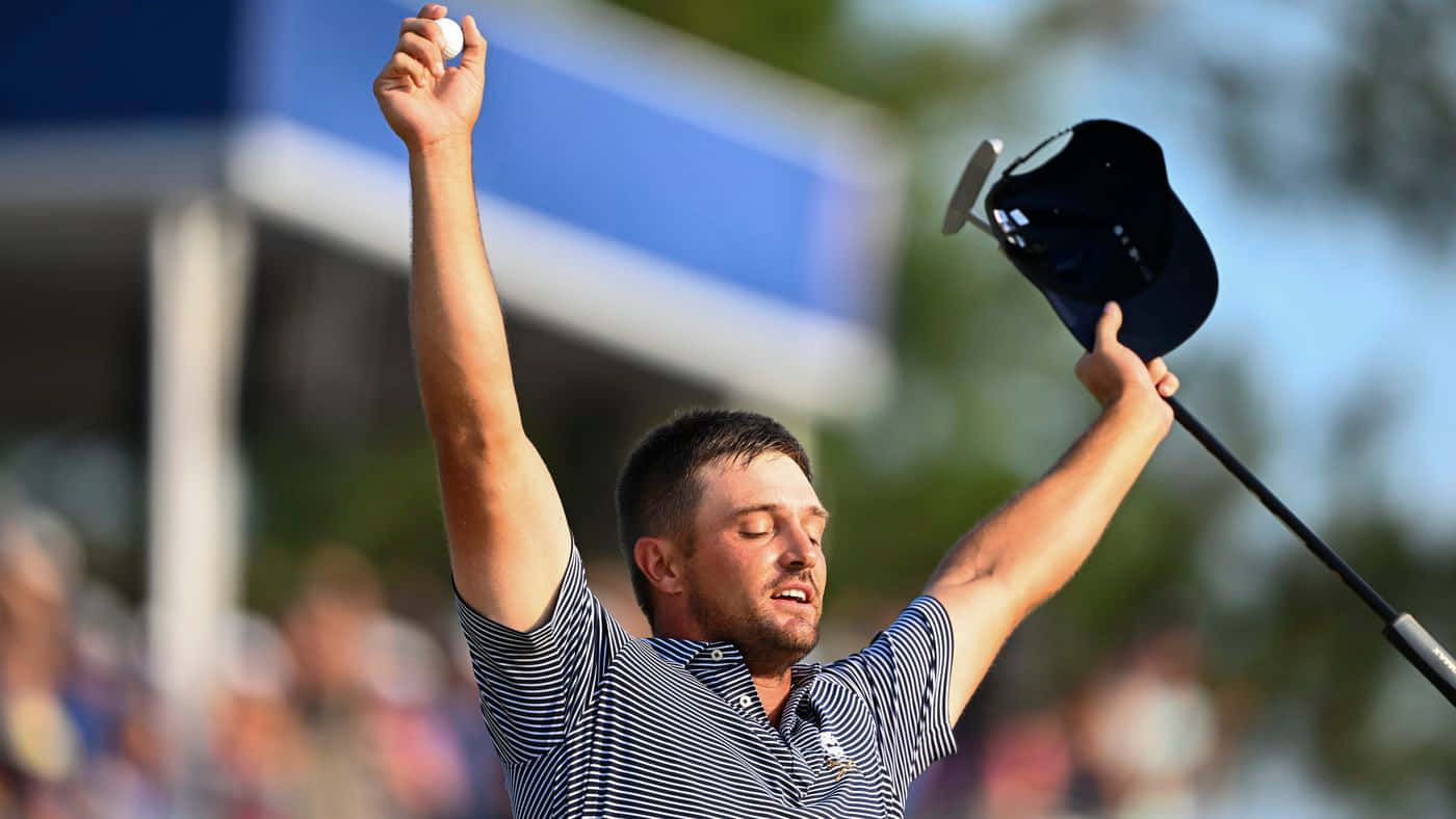  壁紙 — 一位勝利的哥爾夫球手在明亮的日光下高舉拳頭和帽子慶祝勝利，背景是模糊的觀眾。