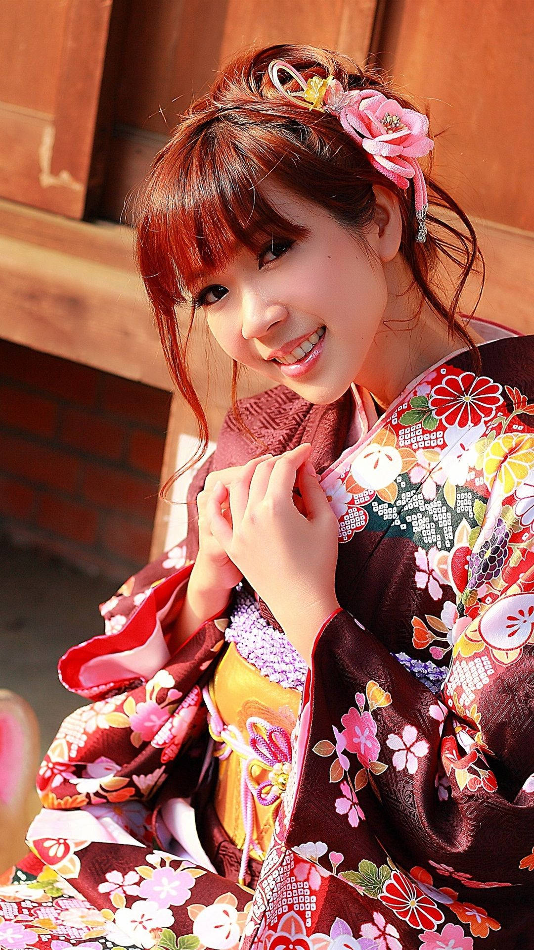 身穿彩色花卉和服的年輕女性在戶外木結構附近微笑。