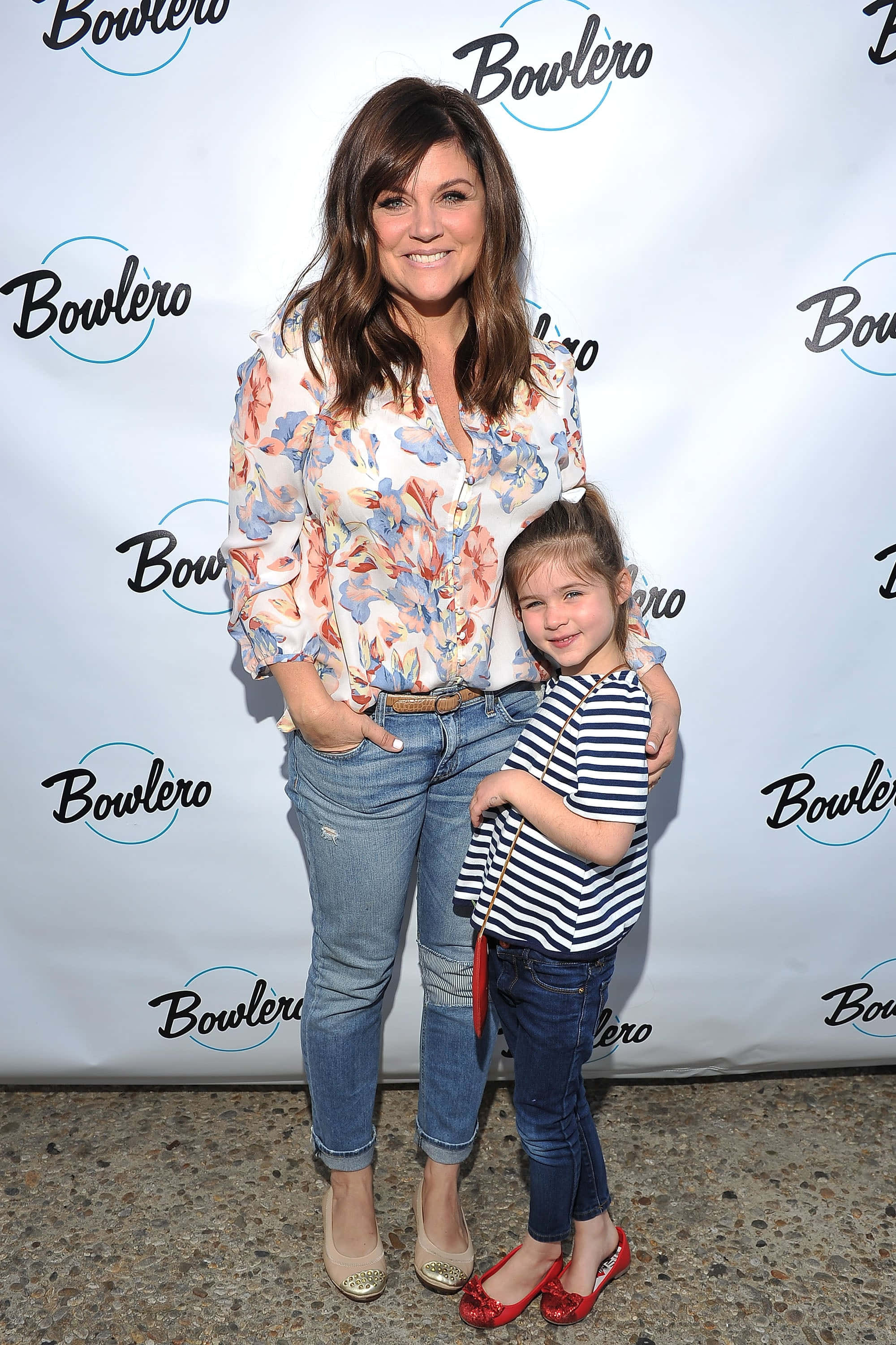 tiffani thiessen 桌布 壁紙 — 一位微笑的女士和年輕女孩在活動中一起在品牌背景前擺姿勢。