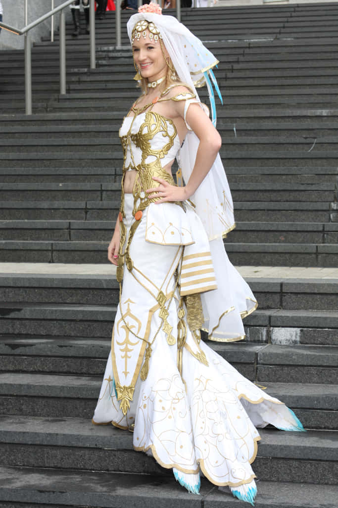 Final Fantasy Ashe 桌布 壁紙 — 一位微笑的女性身穿華麗的白色和金色幻想服裝，在灰色石階上優雅地擺姿勢。