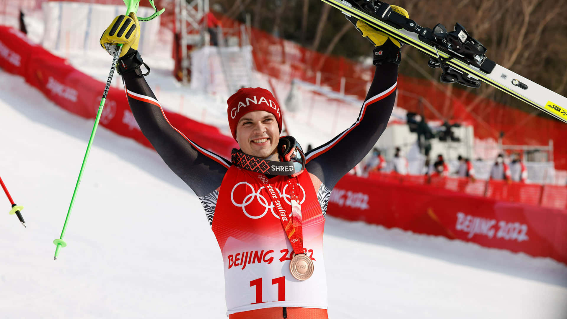  壁紙 — 一位喜悅的加拿大滑雪選手在北京2022年冬奧會上高舉滑雪板，佩戴銅牌慶祝。