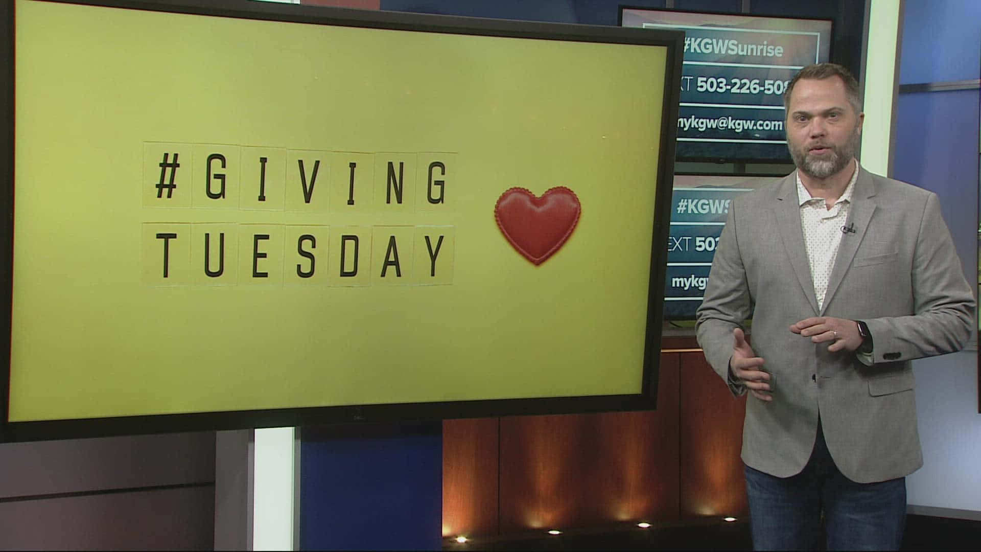  壁紙 — 一位新聞主播站在一個亮黃色屏幕旁邊，屏幕上顯示「#GIVING TUESDAY」並帶有紅色心形圖案。