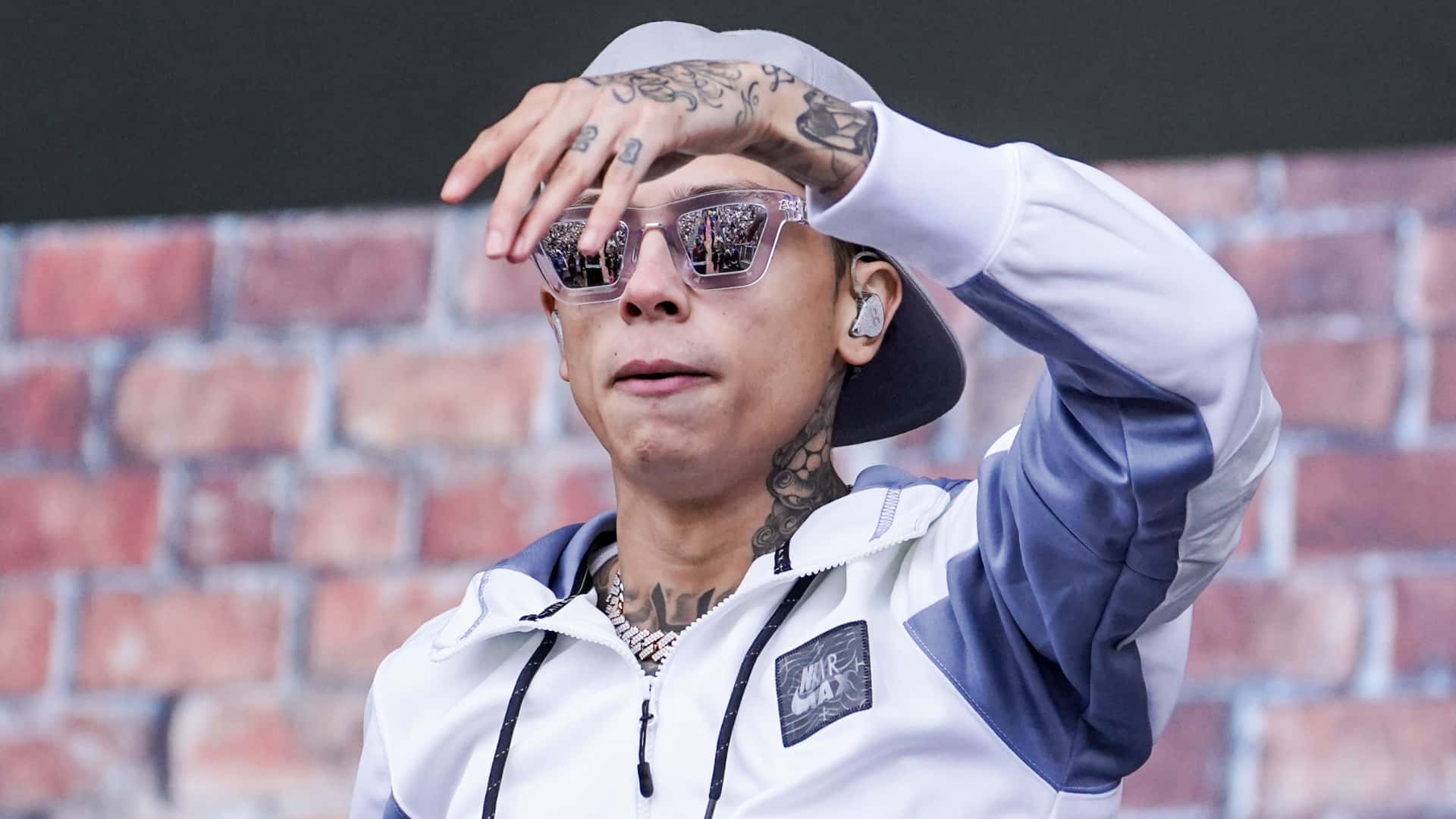  壁紙 — 一位有紋身的男子身穿白色外套和太陽眼鏡，用一隻手遮擋強光保護眼睛。