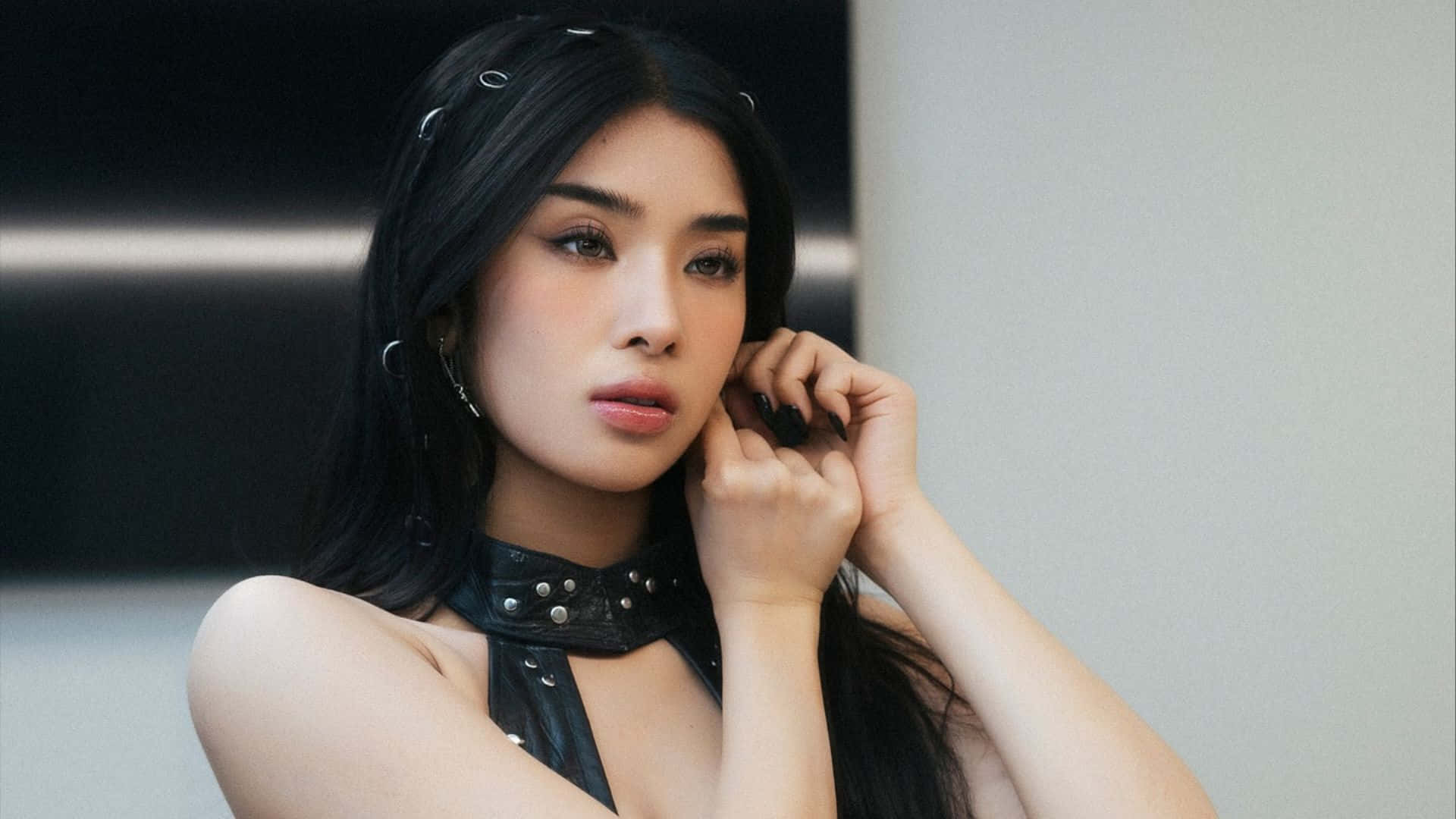  壁紙 — 一位長黑髮、妝容大膽的女性，在現代簡約風格的室內戴著鉚釘皮革頸圈，觸摸耳朵。