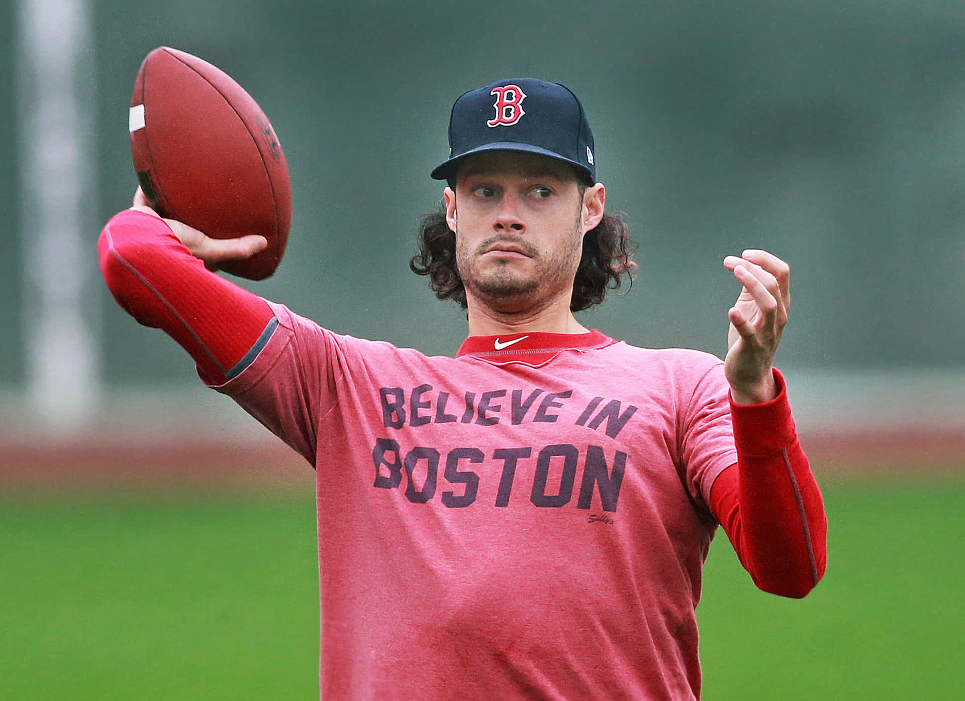  壁紙 — 一位專注的美式足球四分衛，身穿紅色「Believe in Boston」襯衫，準備在綠色球場上擲球。