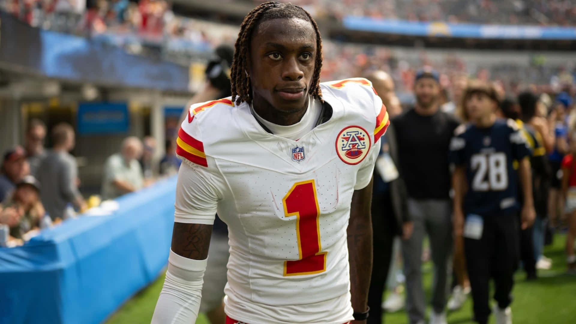  壁紙 — 一位專注的NFL美式足球員身穿白色球衣，紅色一號，在陽光普照的球場上行走。