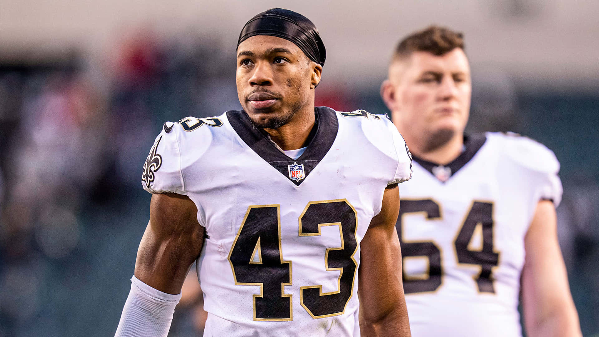  壁紙 — 一位專注的NFL球員身穿白色球衣，號碼43，在比賽中站在球場上，體育場的燈光映照出他堅定的表情。