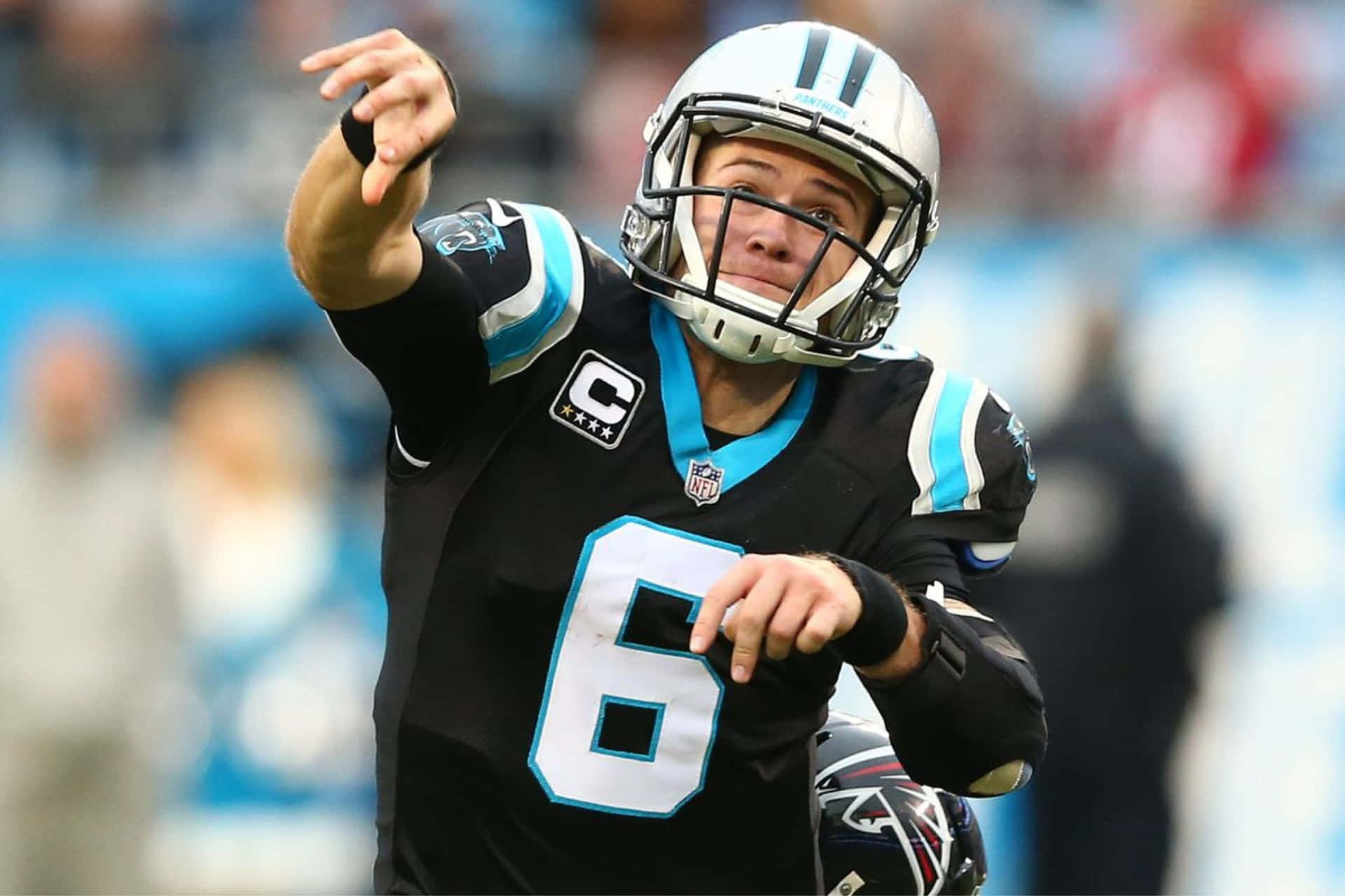  壁紙 — 一位專注的NFL四分衛身穿黑藍色6號球衣，在日間比賽中擲出橄欖球。