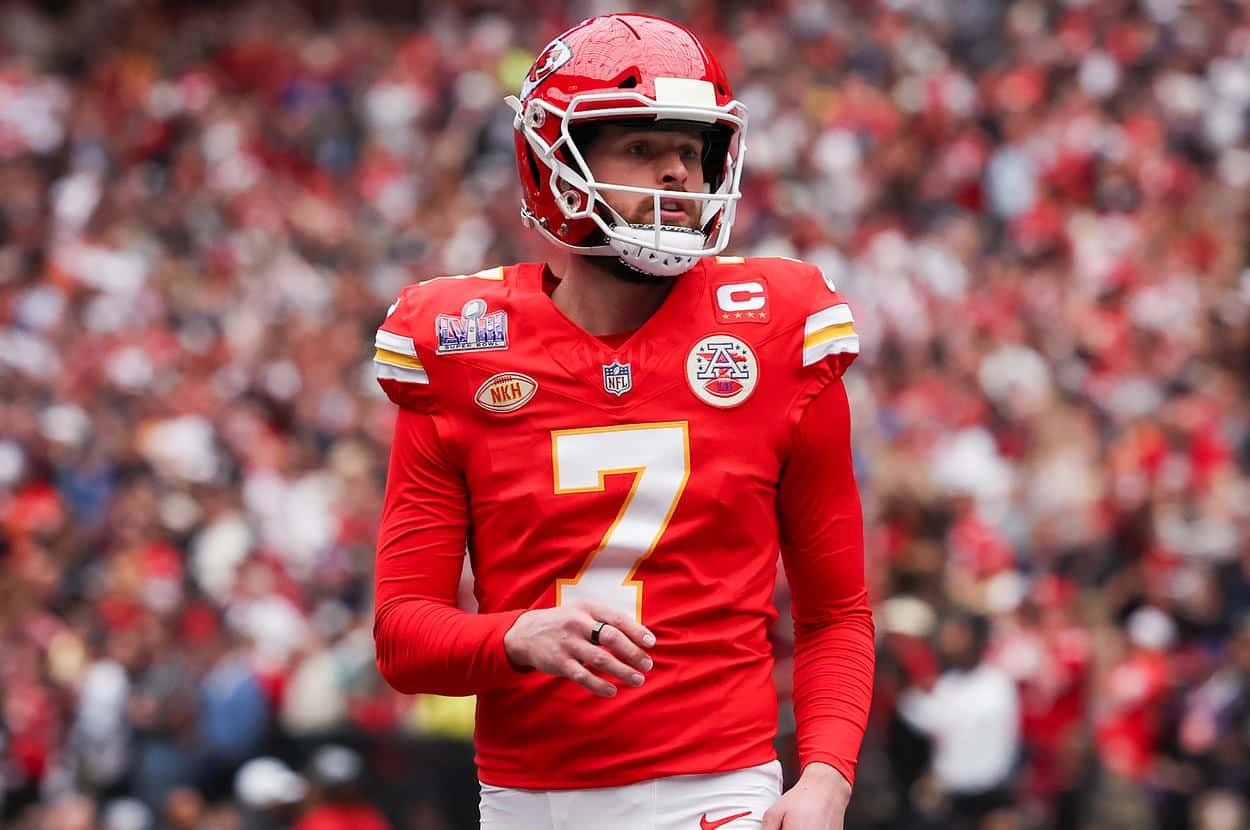 Harrison Butker 桌布 壁紙 — 一位專注的NFL四分衛身穿紅色7號球衣，在比賽中站在球場上，背景是模糊的人群。