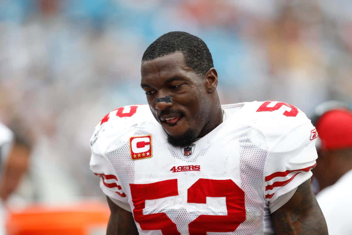  壁紙 — 一位專注的NFL線衛身穿白色和紅色的49號球衣，號碼52，在日間比賽中低頭。