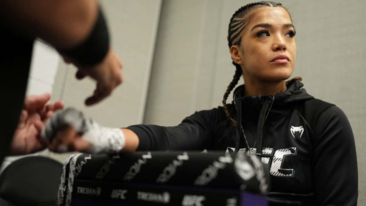  壁紙 — 一位專注的女性MMA拳手，身穿帶有UFC標誌的黑色連帽衫，在訓練前準備她的手，同時專注地看著她的教練。